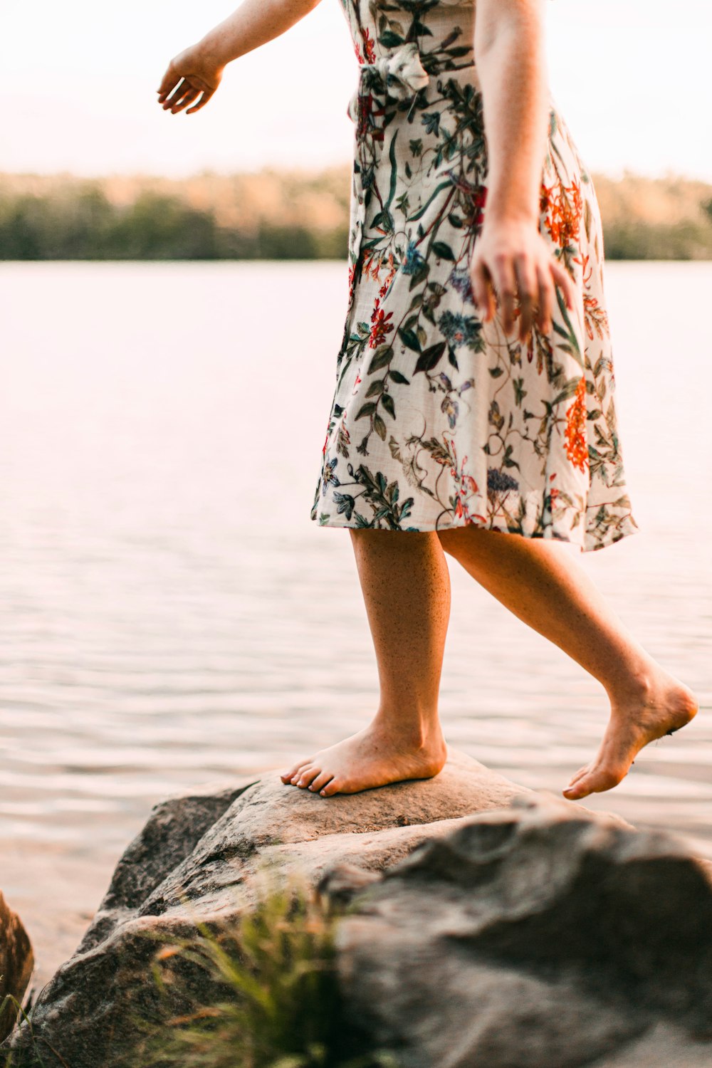 woman in white red and black floral dress standing on gray rock near body of water