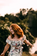 woman in white black and red floral sleeveless dress standing near green trees during daytime