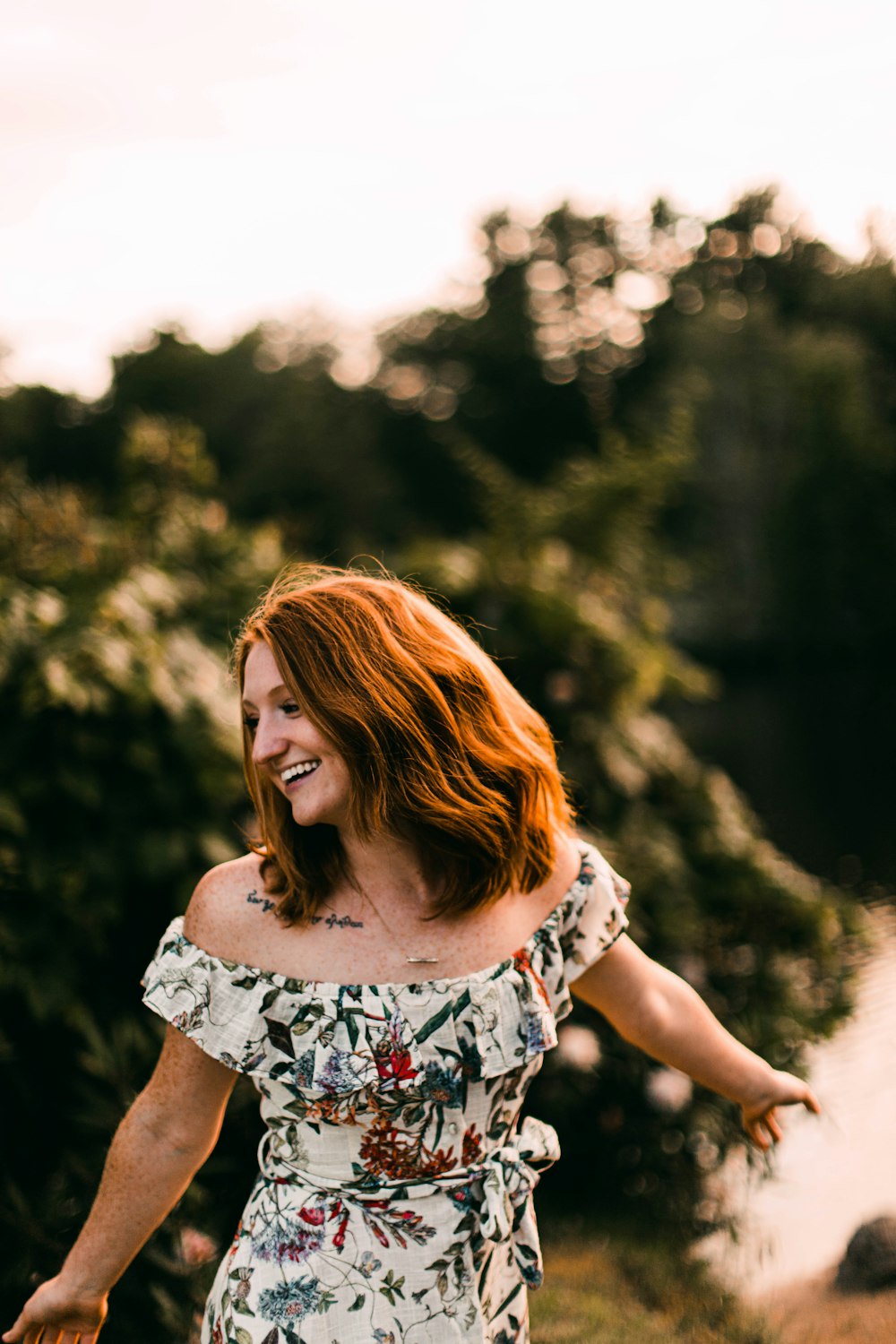 femme en robe sans manches à fleurs blanches, noires et rouges, debout près d’arbres verts pendant la journée