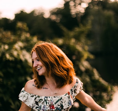 woman in white black and red floral sleeveless dress standing near green trees during daytime