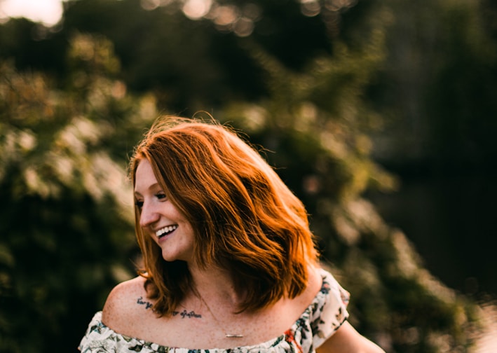 woman in white black and red floral sleeveless dress standing near green trees during daytime