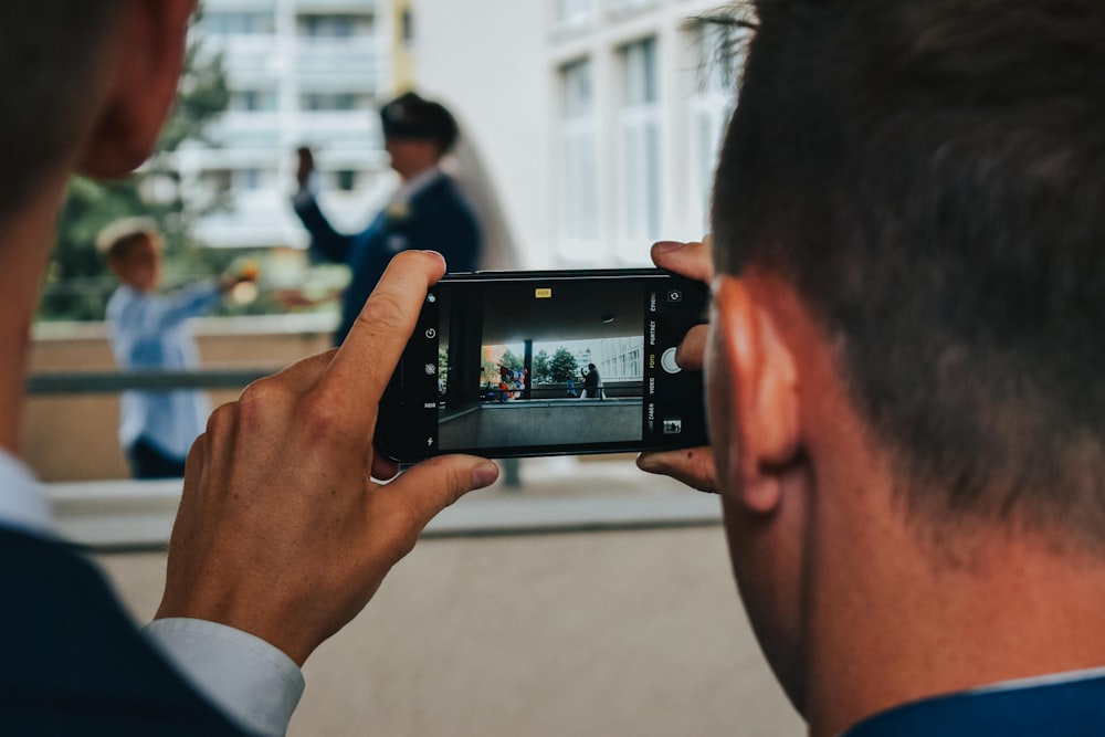 man in white dress shirt holding black smartphone