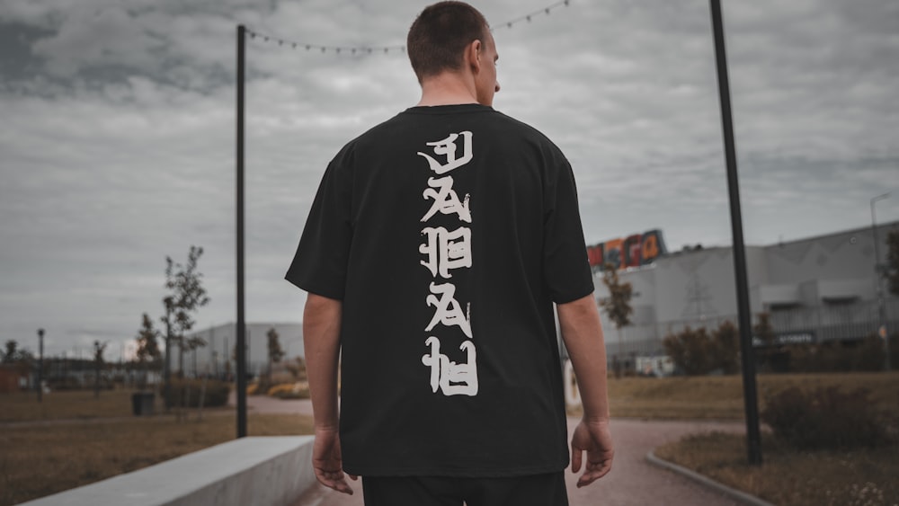 man in black and white crew neck t-shirt standing on gray concrete pavement during daytime