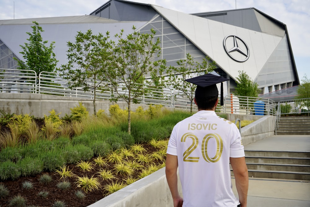 man in white crew neck t-shirt and black cap standing near green plants during daytime