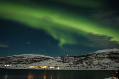 snow covered mountain near body of water during night time