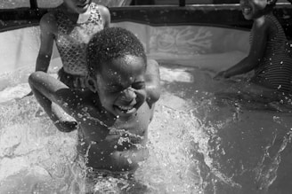 Children playing joyfully with colorful water toys in a sunny backyard pool.