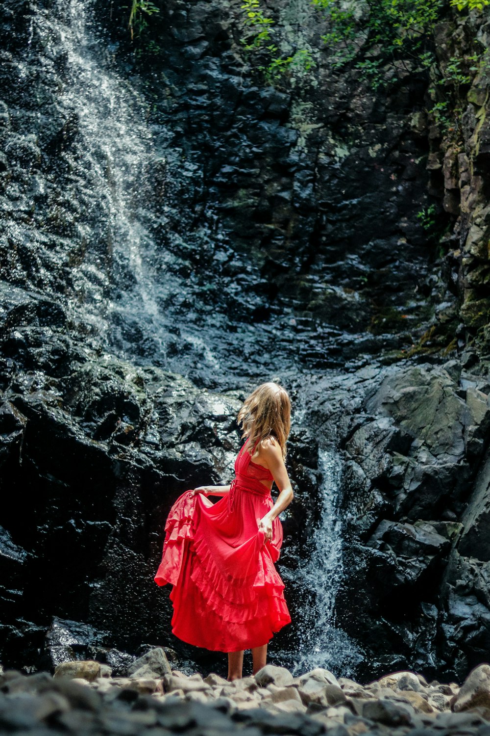 woman in red dress standing on rocky river