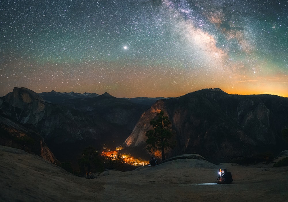 person sitting on ground near bonfire under starry night