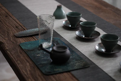 A rustic wooden table set with bright, hand-thrown stoneware cups and a teapot.