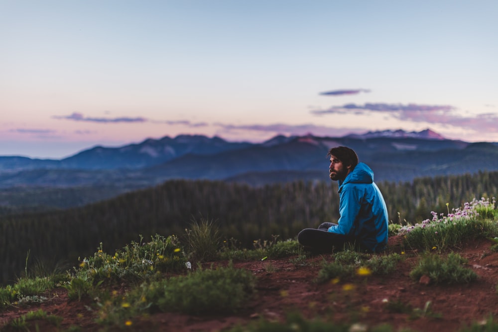 man in teal hoodie sitting on green grass field during daytime