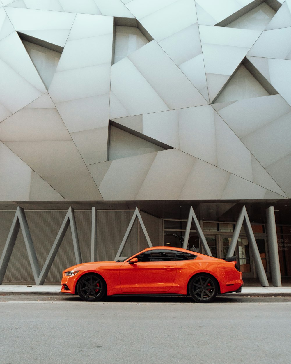 orange coupe parked near gray concrete building