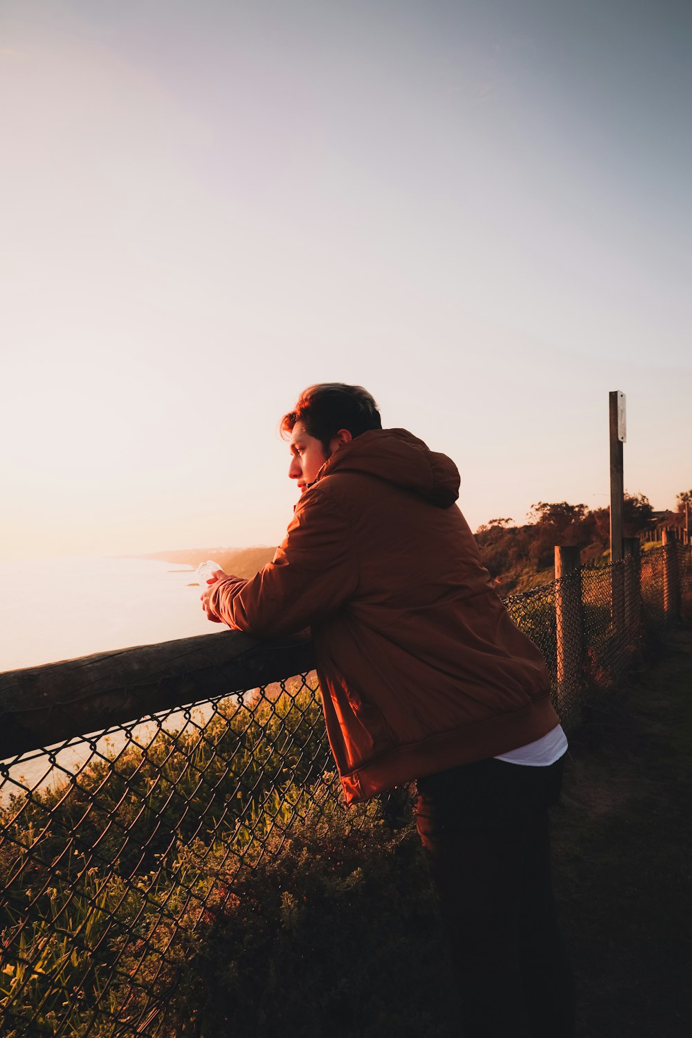 man in brown hoodie standing near brown wooden fence during daytime