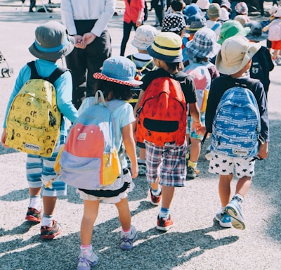 group of people wearing white and orange backpacks walking on gray concrete pavement during daytime