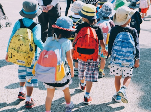 group of people wearing white and orange backpacks walking on gray concrete pavement during daytime