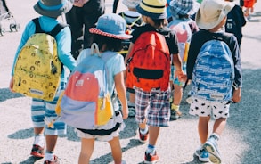 group of people wearing white and orange backpacks walking on gray concrete pavement during daytime