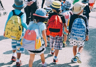 group of people wearing white and orange backpacks walking on gray concrete pavement during daytime