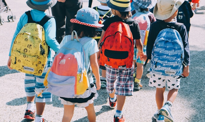 group of people wearing white and orange backpacks walking on gray concrete pavement during daytime