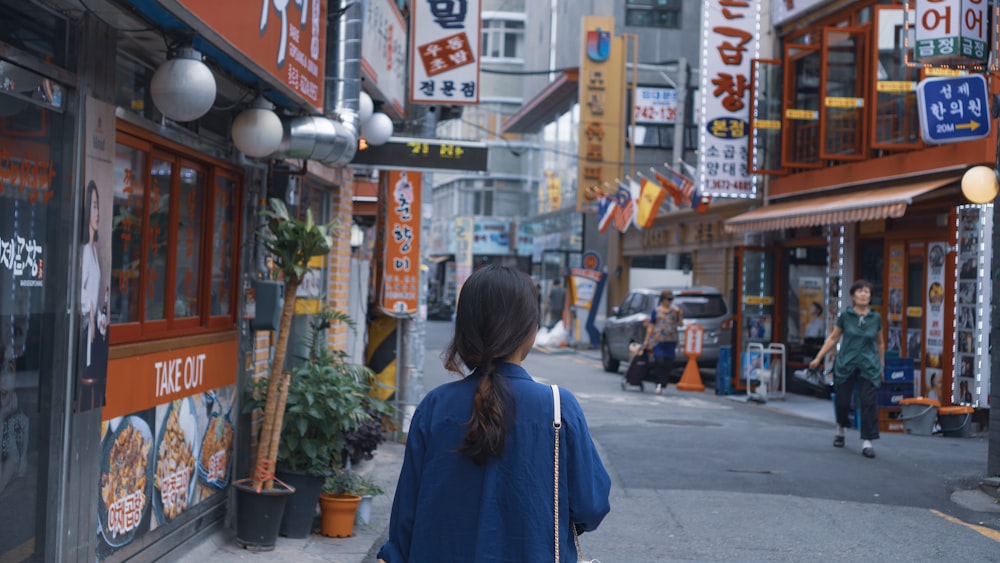 woman in blue long sleeve shirt standing on sidewalk during daytime