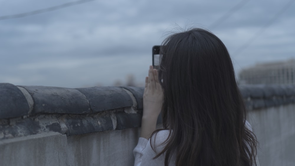 woman in white long sleeve shirt holding black smartphone