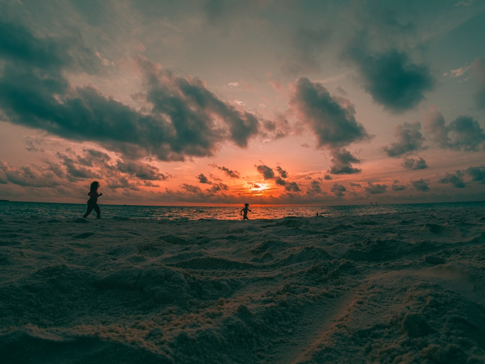 silhouette of 2 people walking on beach during sunset