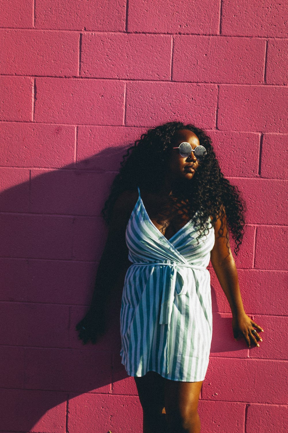 woman in white and blue dress leaning on red brick wall