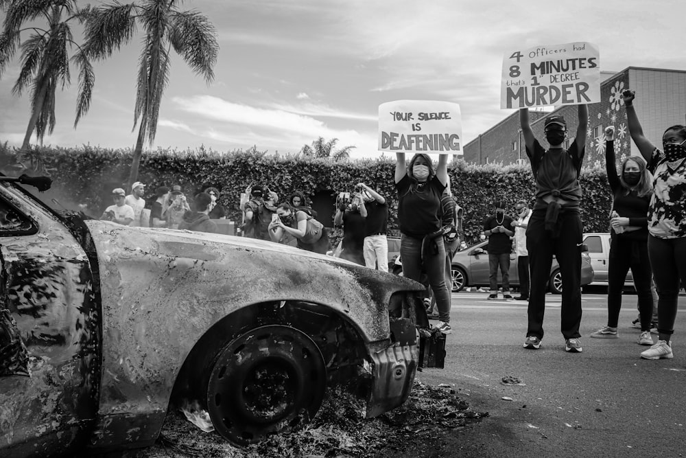 grayscale photo of people standing beside car