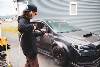 man in black jacket and brown pants standing beside black car during daytime