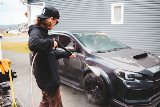 man in black jacket and brown pants standing beside black car during daytime