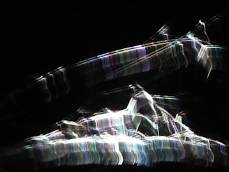 Bright, abstract light patterns create a dynamic array of streaks against a dark background with a chaotic, energetic flow.