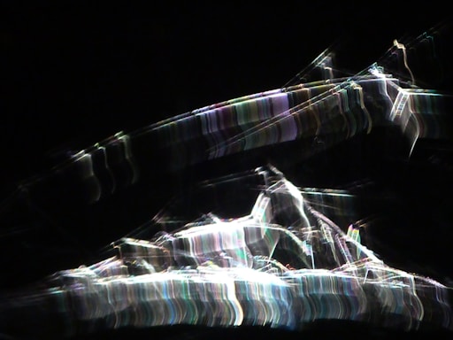 Bright, abstract light patterns create a dynamic array of streaks against a dark background with a chaotic, energetic flow.