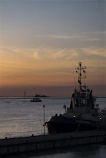 A sturdy tugboat guiding a large vessel through calm ocean waters during sunset.