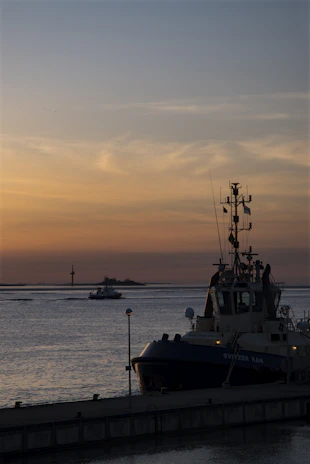 A sturdy tugboat guiding a large vessel through calm ocean waters during sunset.