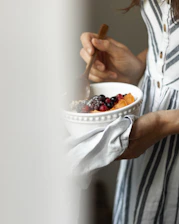 a woman holding a bowl of fruit and a spoon