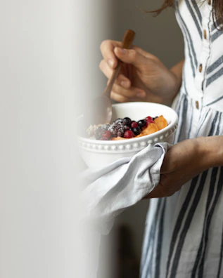 a woman holding a bowl of fruit and a spoon