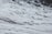 A group of people wearing colorful jackets and hiking gear is trekking across a vast snow-covered glacier. The landscape is dominated by icy, rugged terrain with patches of rock and ice.