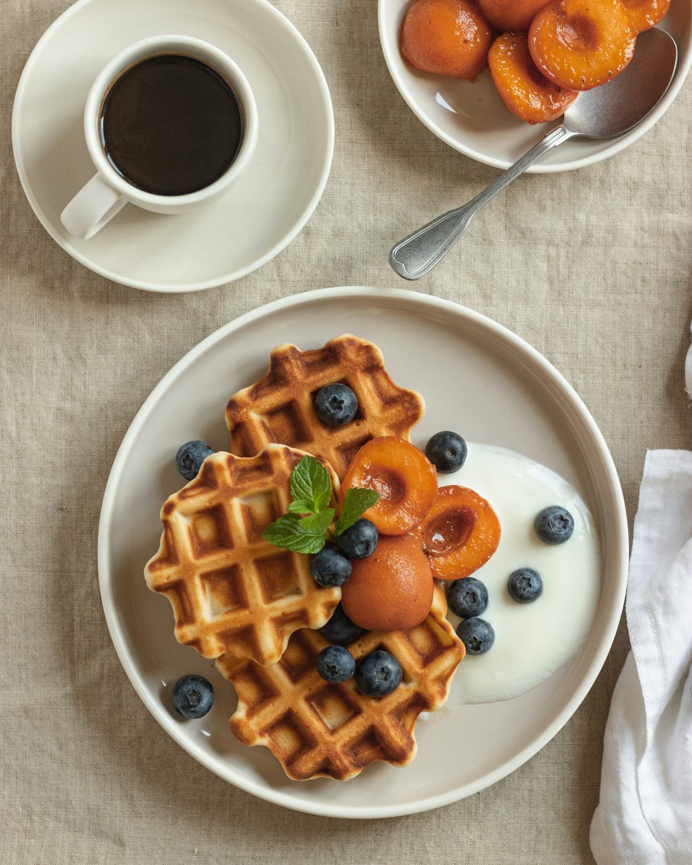 waffle with strawberry on white ceramic plate beside stainless steel spoon and white ceramic mug with on on on on