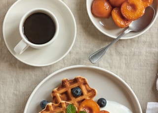 waffle with strawberry on white ceramic plate beside stainless steel spoon and white ceramic mug with on on on on