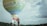 Two people are preparing a hot air balloon with 'wonderful Indonesia' written on it. The balloon is set against a backdrop of a cloudy sky and some distant foliage.
