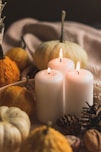 white pillar candle beside orange pumpkin and white pumpkin