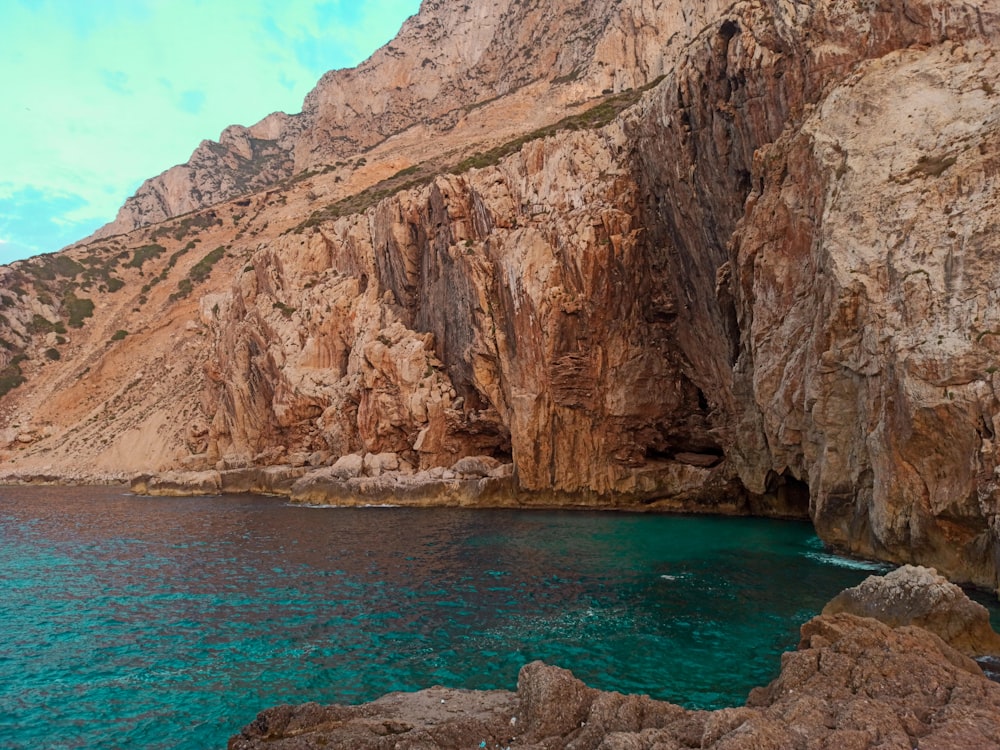 brown rocky mountain beside blue sea under blue sky during daytime