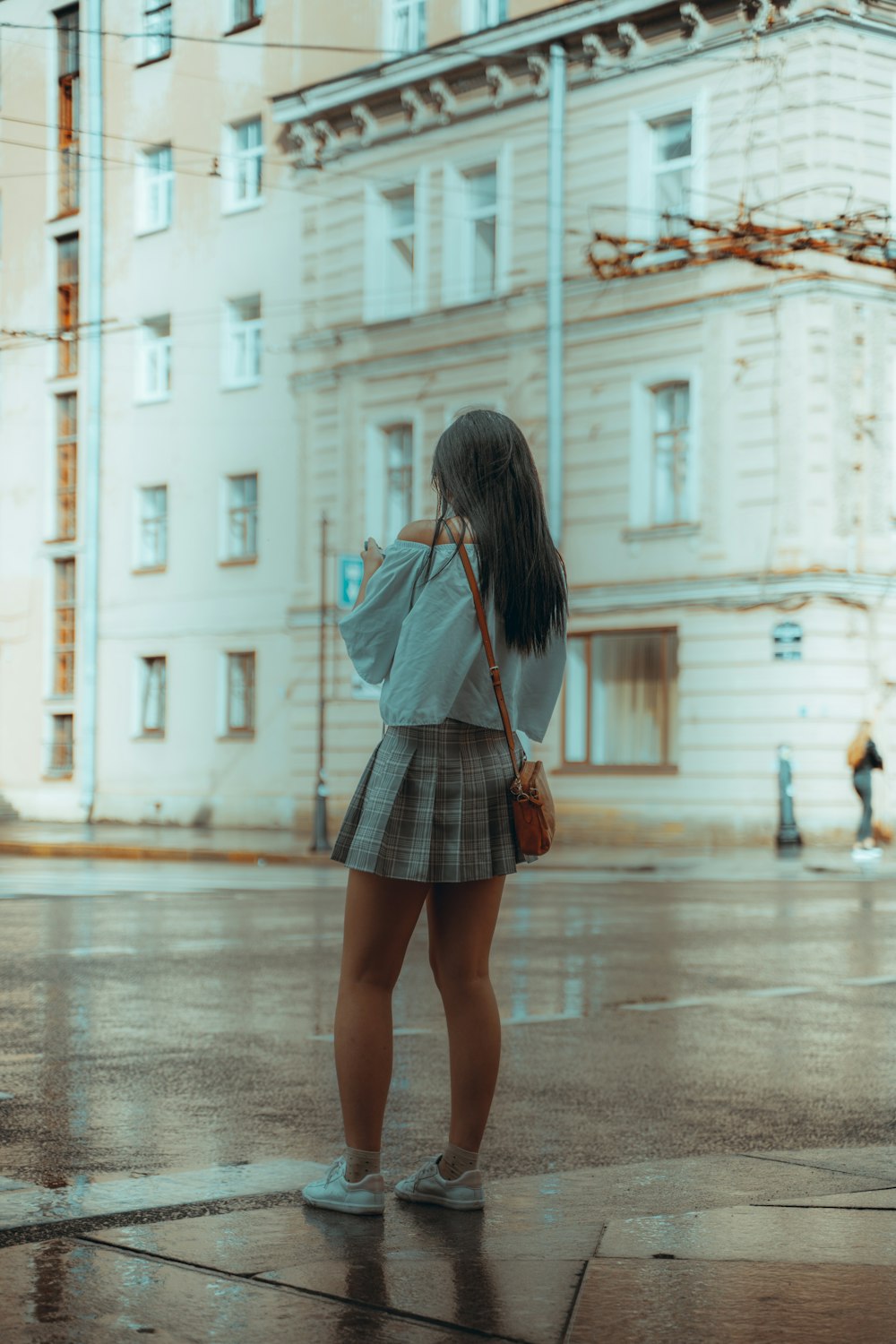 woman in gray long sleeve shirt and black and white plaid skirt walking on sidewalk during