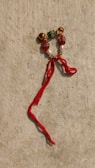 A decorative piece composed of beads and small bells arranged in a circular pattern, with a notable red thread tied onto it, lying on a textured, beige surface.