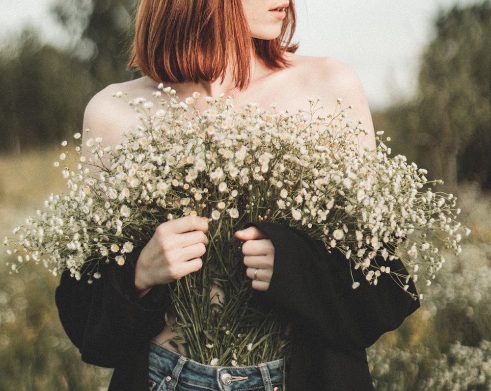 woman in white floral off shoulder shirt and blue denim jeans holding white flowers