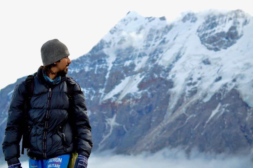 man in black jacket and black knit cap standing on snow covered ground