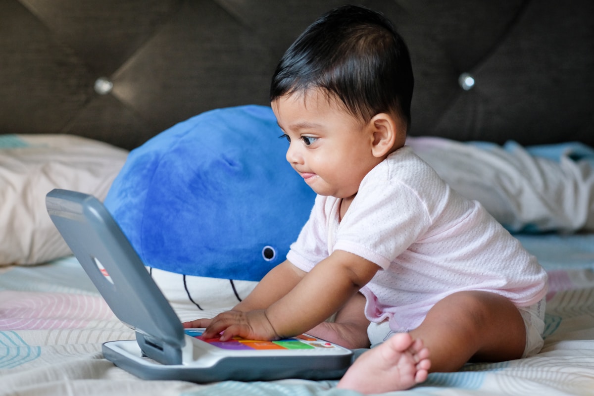 baby in pink shirt sitting on blue textile