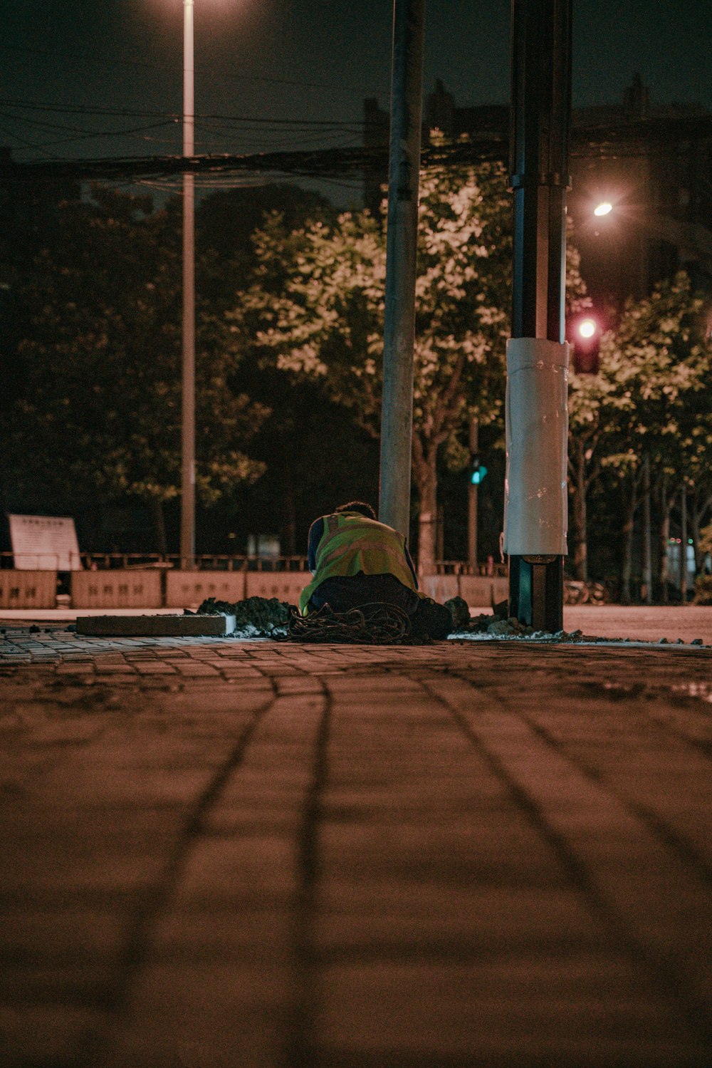 person in green jacket sitting on sidewalk during night time