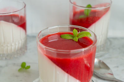 Colorful panna cotta in glass jars topped with raspberry sauce and delicate edible flowers.