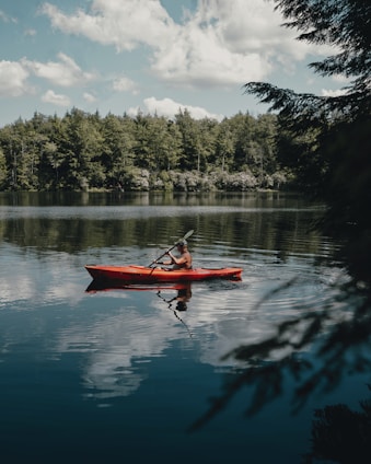 person riding red kayak on lake during daytime