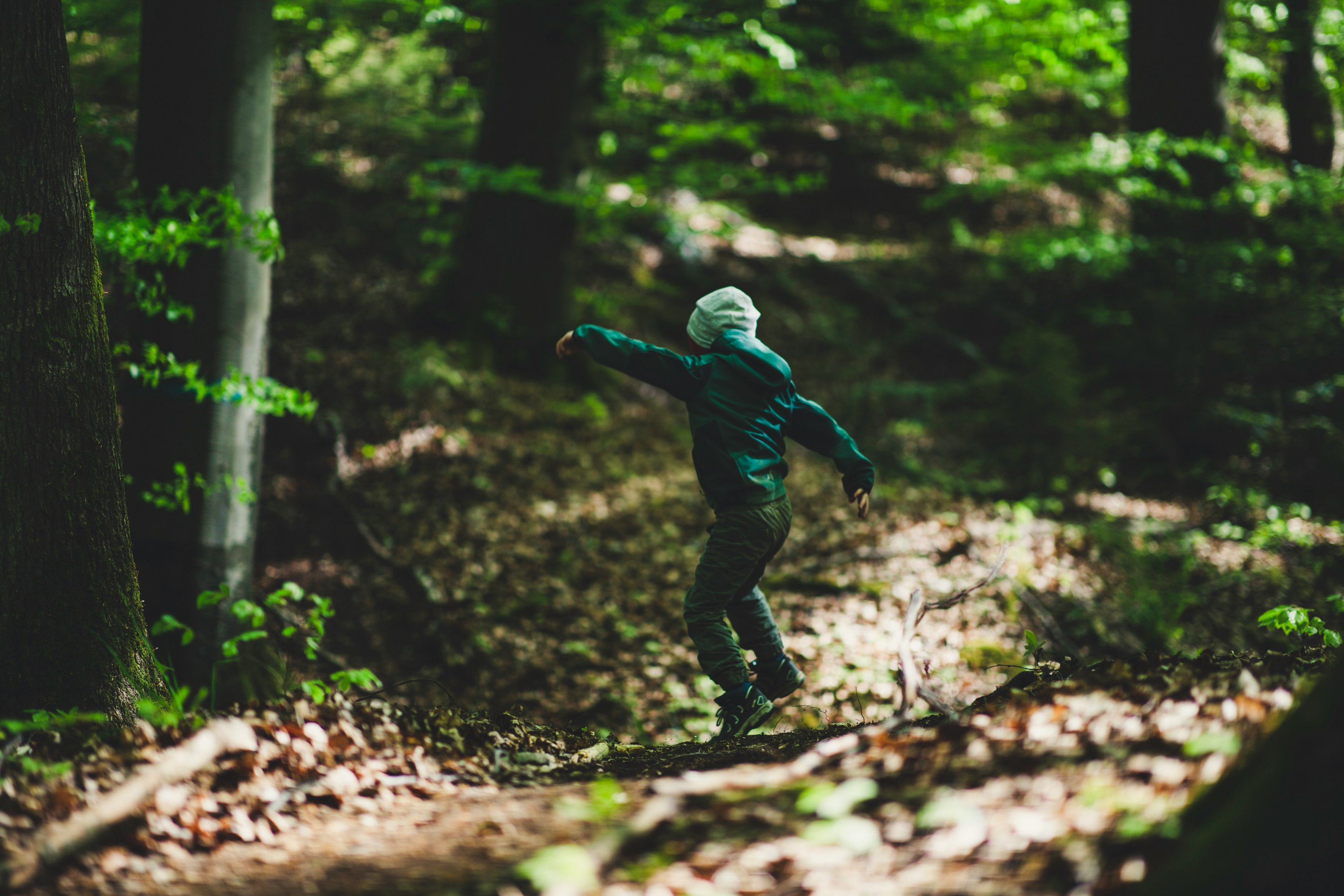 man in blue jacket and black pants jumping on tree trunk during daytime