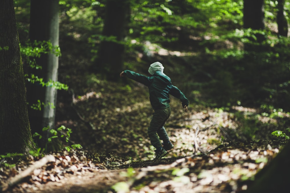 man in blue jacket and black pants jumping on tree trunk during daytime